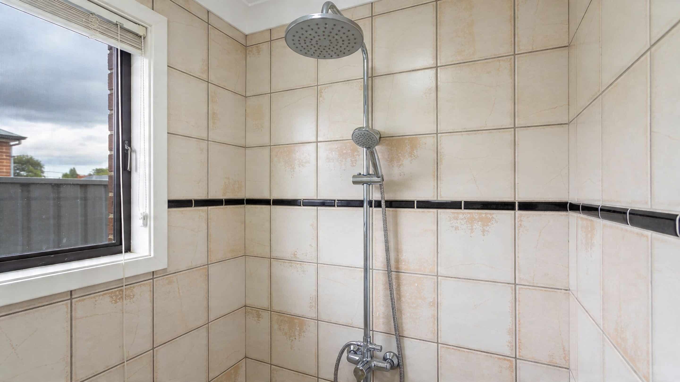 A tiled bathroom shower stall featuring a chrome shower head and a decorative black border tile.